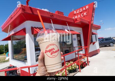 Rudyard, Montana - 2 juillet 2022 : la main tient un cocktail de chocolat au restaurant Sugar Shack du restaurant rétro à l'arrière-plan sur la chaîne (ou US-2) Banque D'Images