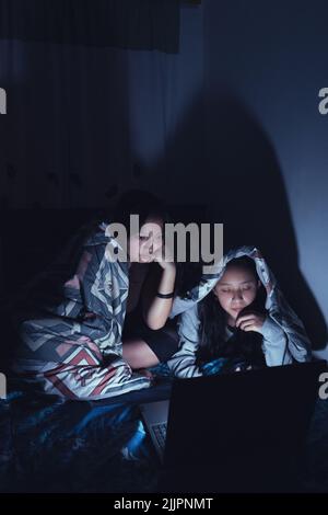 Photo verticale de deux jeunes femmes hispaniques dans un traîneau regardant des films dans la nuit sur un ordinateur portable Banque D'Images