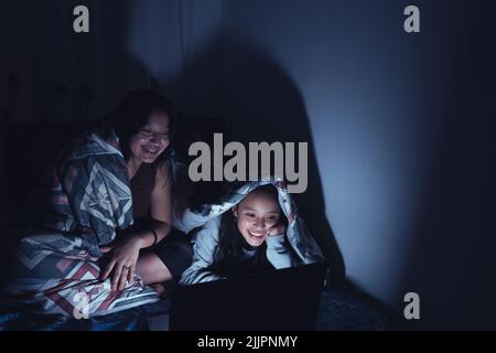 Photo verticale de deux jeunes femmes hispaniques dans un traîneau regardant des films dans la nuit sur un ordinateur portable Banque D'Images