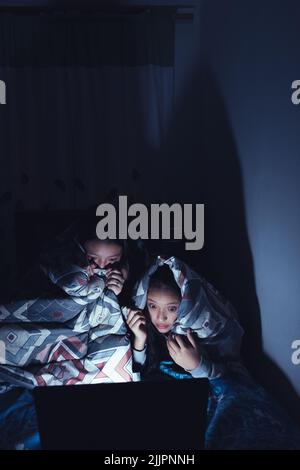 Photo verticale de deux jeunes femmes hispaniques dans un traîneau regardant des films dans la nuit sur un ordinateur portable Banque D'Images