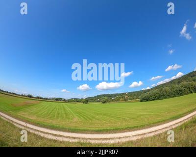 Une vallée ouverte avec une végétation luxuriante entourée de collines sur un fond bleu ciel nuageux Banque D'Images