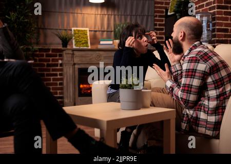 Les personnes frustrées se battant à la séance de thérapie de couple avec un spécialiste, ayant des arguments sur les difficultés de mariage. Essayer de résoudre les problèmes de relation avec les conseils professionnels de thérapeute. Banque D'Images