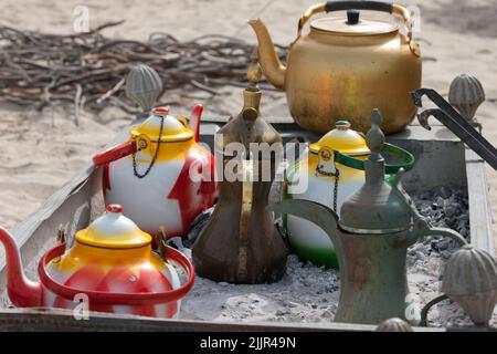 Pots à thé arabes variables debout dans les cendres froides du feu. L'arbre brunit à l'arrière-plan pour un feu Banque D'Images