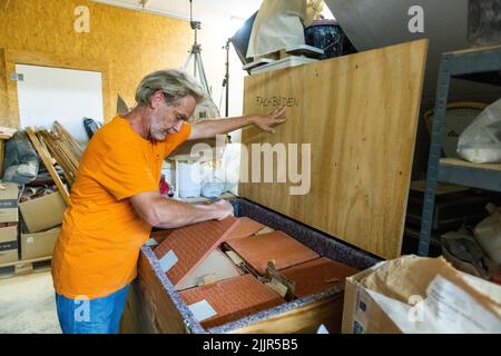 Buggingen, Allemagne. 25th juillet 2022. Andreas Benrath sort une plaque en céramique d'une boîte dans son atelier. Le céramiste A. Benrath a transformé le célèbre roman de S. Nadolny « la découverte de la lenteur » en un monument en argile battue. Au cours de deux bonnes années de travail, Benrath a transféré l'histoire de l'explorateur polaire britannique J. Franklin (1786-1847), qui est mort pendant une expédition, sur des plaques d'argile dans son atelier de Buggingen. Credit: Philipp von Ditfurth/dpa/Alay Live News Banque D'Images