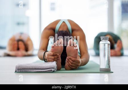 Tenir et respirer. Un groupe méconnaissable de femmes pratiquant le yoga et tenant une posture assise repliée vers l'avant. Banque D'Images