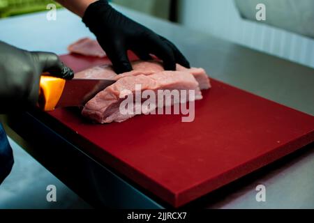 Gros plan d'une personne coupant de la viande crue Banque D'Images