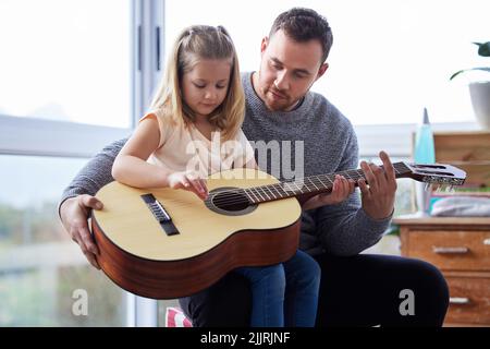 Elle lui enseignait des accords. Un jeune père enseignant à sa fille de jouer de la guitare à la maison. Banque D'Images