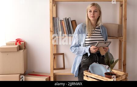 Bonne fille regardant le cadre photo, partageant des souvenirs, debout dans le salon, jeune femme déballant des boîtes en carton avec des effets personnels le jour de déplacement Banque D'Images