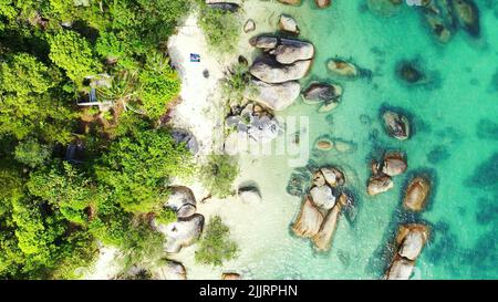 Une vue aérienne d'une plage avec des arbres, de grands rochers et de l'eau turquoise aux Maldives Banque D'Images