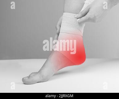 Femme enveloppant un bandage élastique autour de la cheville douloureuse pour réduire la douleur et l'inflammation du talon. Pieds avec point rouge. Fasciite plantaire, traitement tendinite. Concept de soins de santé. Noir et blanc. Photo Banque D'Images