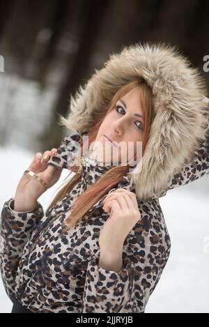 Portrait d'une jeune femme du caucase portant un manteau d'hiver à imprimé léopard dans un parc enneigé Banque D'Images