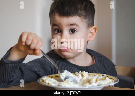 Enfant dans la cuisine pendant la journée manger des pâtes à la table, regardant l'appareil photo. Une alimentation saine. Repas sain. Banque D'Images