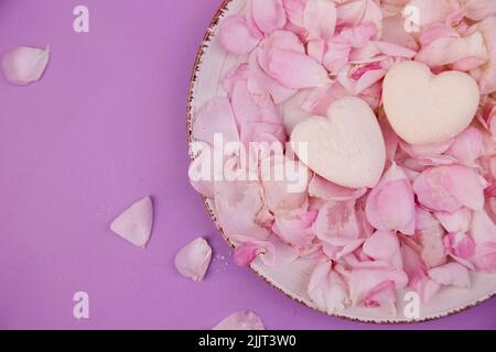 Guimauves naturelles sans sucre vanillé coeurs sur pétales de rose. Bonbons sains, nourriture naturelle. Arrière-plan romantique. Banque D'Images