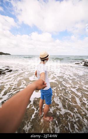 Jeune homme tenant la main de son petit ami quand ils marchent sur la plage Banque D'Images