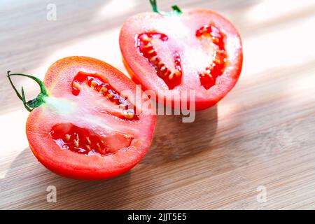 Gros plan de la moitié coupée de deux tomates juteuses rouges sur une planche à découper en bois, deux tomates coupées fraîches à la lumière du jour. Banque D'Images