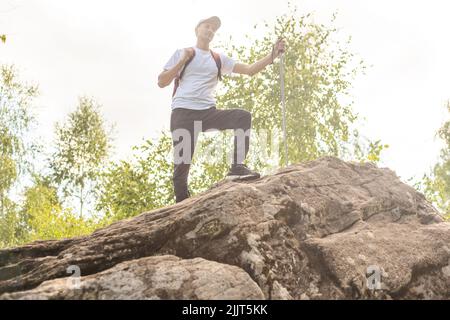 Jeune randonneur avec sac à dos et bâtons de randonnée debout sur le bord de la falaise et regardant les montagnes en été en plein air. Banque D'Images