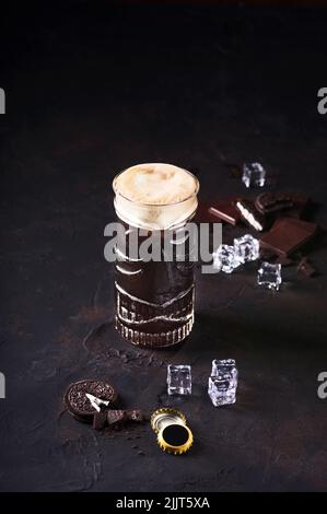 Pinte de bière foncée avec glace, chocolat et gâteau de Savoie sur fond sombre, servir dans américain traditionnel. Bière filtrée foncée Banque D'Images