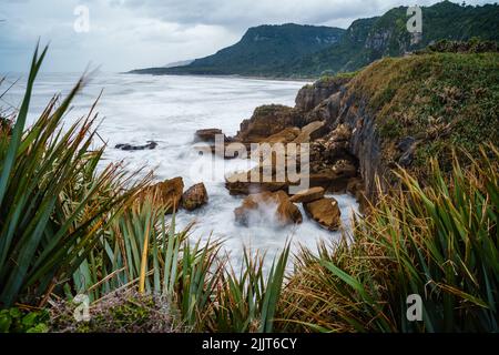 Une vue à couper le souffle depuis le rivage d'eau mousseuse avec des collines en arrière-plan à Pancake Rocks, Westport, Nouvelle-Zélande Banque D'Images