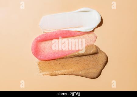 trois types de gommage du visage sur fond beige. Échantillon de peeling de peau de corps de visage. Café, fraise et gommage crémeux Banque D'Images