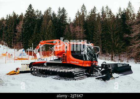 Une tondeuse à neige Pisten Bully garée sur une piste de ski près d'une forêt Banque D'Images