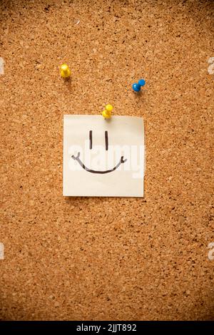 Un morceau de papier avec une épingle à visage smiley sur un corkboard Banque D'Images