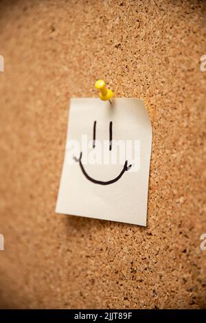 Un morceau de papier avec une épingle à visage smiley sur un corkboard Banque D'Images