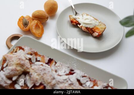 tarte rectangulaire appétissante à l'abricot maison sur une plaque rectangulaire, sur une planche à découper en bois. À côté est une assiette ronde avec un morceau de gâteau et un Banque D'Images