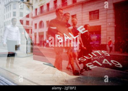 Les passants masculins et un détail d'un feuillet déchu décrivant la vente de costumes pour hommes, dans une entreprise fermée de vêtements dans la City de Londres, le quartier financier de la capitale, le 27th juillet 2022, à Londres, en Angleterre. Banque D'Images