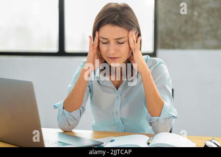 Portrait de la jeune femme employée avec des maux de tête frottant ses temples surtravaillé femme Banque D'Images