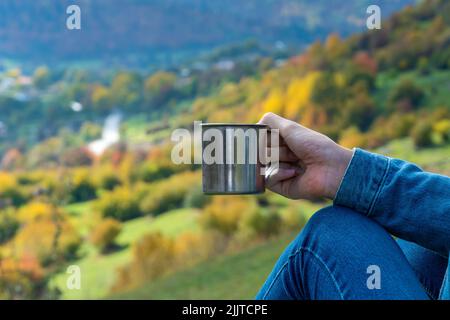 Gros plan de la main d'une femme tenant une tasse de métal avec café ou thé sur le fond des montagnes.Concept de voyage, de camping, de mode de vie actif Banque D'Images