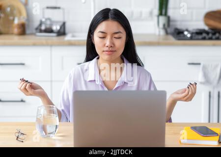 Jeune femme freelance avec ordinateur portable méditant les yeux fermés pensant à de bonnes choses Banque D'Images