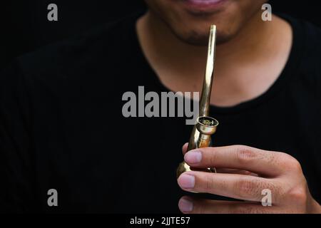 L'homme asiatique fume de la marijuana dans une pipe à la maison. Studio Shoot avec modèle simulant pot à fumer avec un tuyau dans un arrière-plan sombre. Légalisation du cannabis Banque D'Images