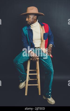 Un homme américain d'origine africaine dans un chapeau et une tenue décontractée posé dans un studio de photo Banque D'Images