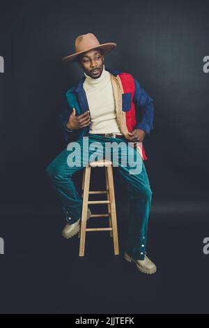Un homme américain d'origine africaine dans un chapeau et une tenue décontractée posé dans un studio de photo Banque D'Images