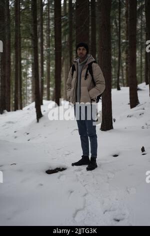 Photo verticale d'un jeune homme caucasien debout sur un sentier de neige dans une forêt d'hiver Banque D'Images