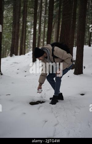 Photo verticale d'un jeune homme caucasien faisant une boule de neige dans une forêt d'hiver Banque D'Images