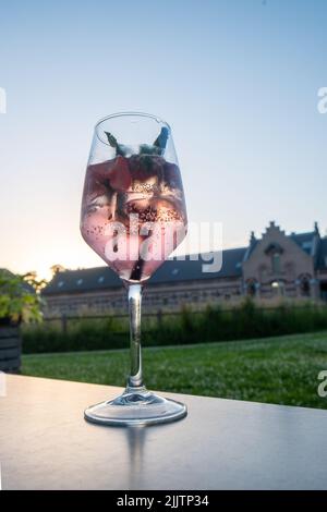 Cocktail rose, cocktail de mocktail ou autre boisson alcoolisée sur la table près des bâtiments historiques du parc et nuage de coucher de soleil dans un cadre rural. Photo de haute qualité Banque D'Images