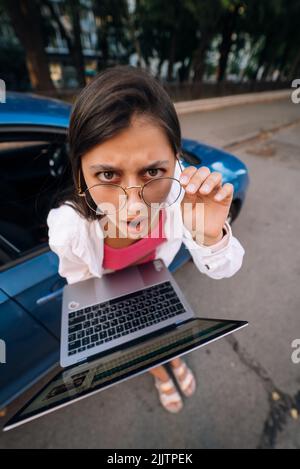 Un jeune brunette choqué tient dans les mains un ordinateur portable dans la rue Banque D'Images