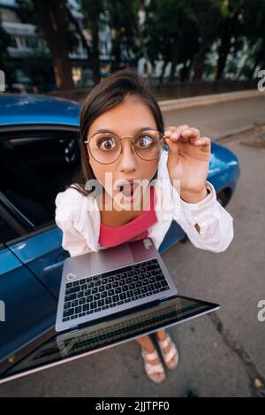 Un jeune brunette choqué tient dans les mains un ordinateur portable dans la rue Banque D'Images