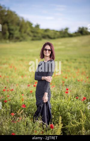 Un beau portrait d'une jeune femme caucasienne debout dans un champ avec des fleurs rouges un jour ensoleillé Banque D'Images