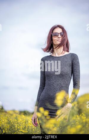 Un beau portrait d'une jeune femme caucasienne se tenant parmi les fleurs jaunes en fleurs dans le champ, par une journée ensoleillée Banque D'Images