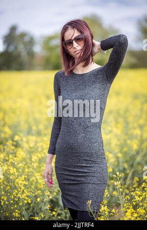 Une belle jeune femme caucasienne posant devant l'appareil photo tout en se tenant parmi les fleurs jaunes en fleurs dans le champ, un jour ensoleillé Banque D'Images