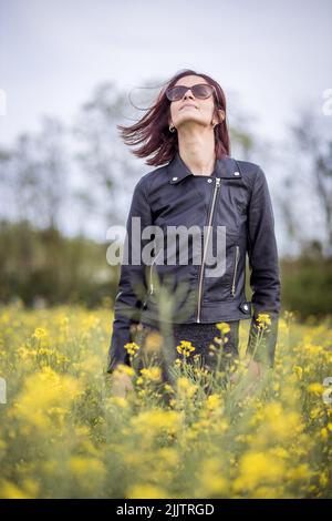 Une belle jeune femme caucasienne se tenant parmi les fleurs jaunes en fleurs dans le champ par un jour ensoleillé Banque D'Images