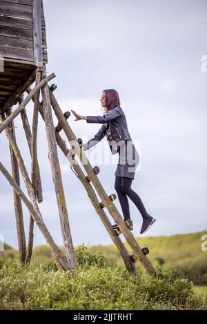 Une belle photo d'une jeune femme caucasienne se montant sur l'échelle d'une ancienne tour de guet en bois dans le parc contre un ciel nuageux par une journée ensoleillée Banque D'Images