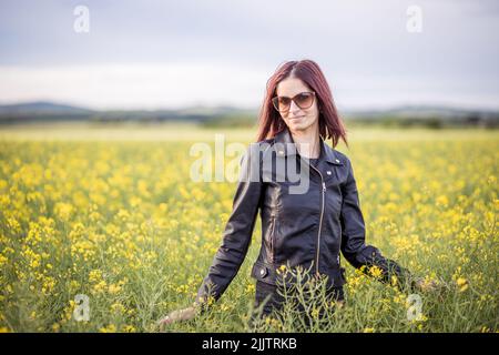 Un beau portrait d'une fille caucasienne debout parmi des fleurs jaunes dans le champ, un jour ensoleillé avec un arrière-plan flou Banque D'Images