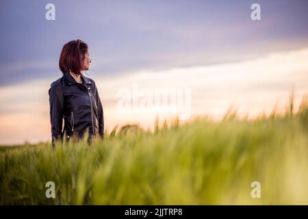 La jeune femme dans une veste de cuir debout dans le champ vert regardant à gauche. Banque D'Images