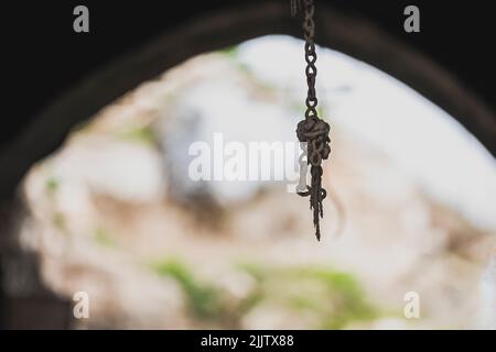 Une ancienne chaîne en métal rouillé accrochée devant une vieille porte avec la lumière du soleil Banque D'Images