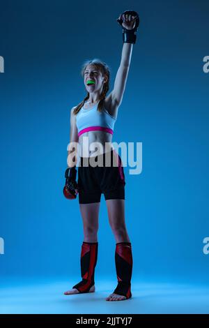 Un combattant MMA junior en uniforme sportif posé isolé sur fond bleu. Concept de sport, compétition, action, mode de vie sain. Banque D'Images