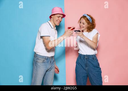 Portrait de jeune couple célébrant l'événement, clinking verres à cocktail, posant isolé sur fond rose bleu studio Banque D'Images