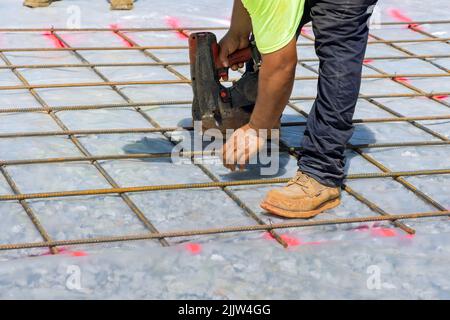 L'ouvrier de la construction torde barres d'acier avec renforcement de tige de fil dans des fondations de ciment à l'aide d'un outil appelé outil de ficelage de barre d'armature. Banque D'Images